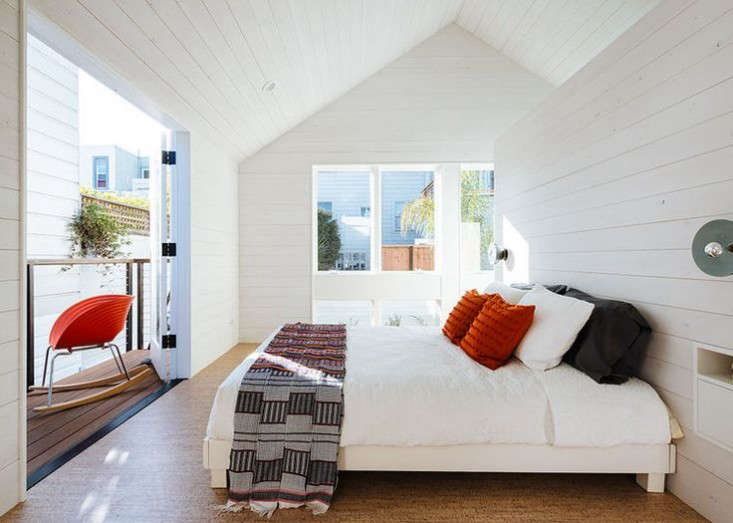 The master bedroom opens to a steel balcony. A freestanding paneled wall divides the space from the bathroom. 