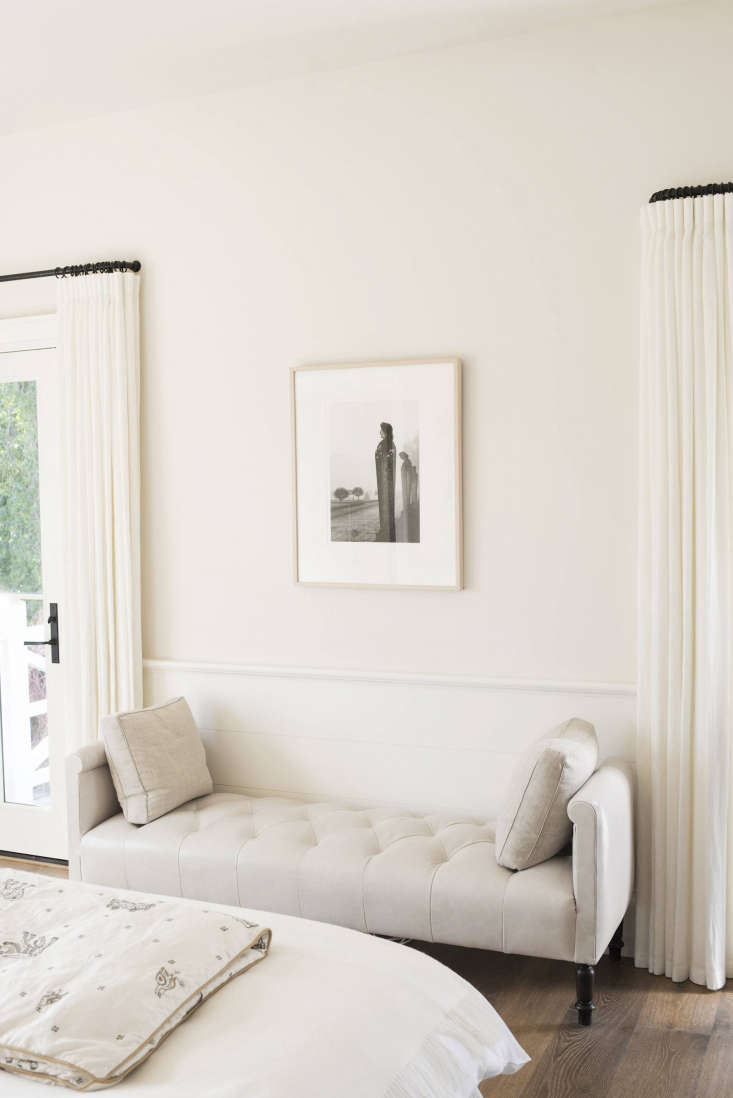 A chaise sits opposite the bed, flanked by two doors leading to a white-painted deck. The rooms on this floor are painted in Farrow & Ball’s Lime White and Slipper Satin.