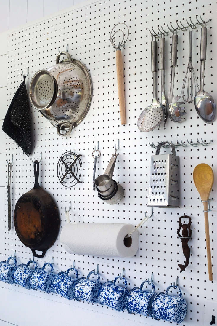 Sourced from a local hardware store, a white pegboard kitted with hooks holds kitchen utility goods. Key features are a row of Blue Splatter Enamel Mugs ($7.99 at Rove & Swig) and a paper towel holder made from spliced marine rope (the contractor made the knot).